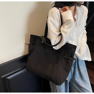 On-body shot of a large black canvas tote bag with drawstring pockets for daily commute