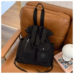 Black versatile drawstring bucket bag with side pocket on a leather sofa
