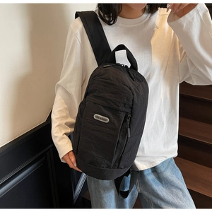 Detail of black nylon chest bag with silver logo tag worn by a model on stairs