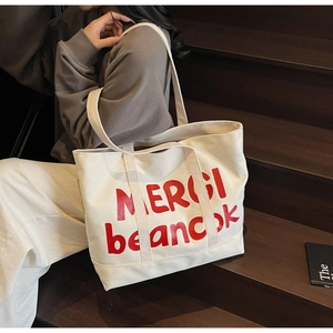 Detail of white canvas tote bag with red letter print and double shoulder straps