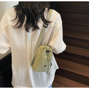 Détail du sac à bandoulière à cordon vert clair en nylon imperméable sur une chemise en lin