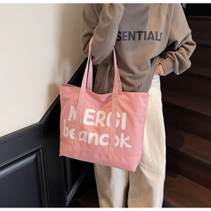 Detail of pink canvas tote bag with MERCI print carried by a model on wooden stairs
