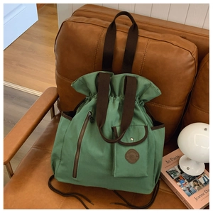 Detail of dark green canvas bucket bag with brown straps on a leather chair background