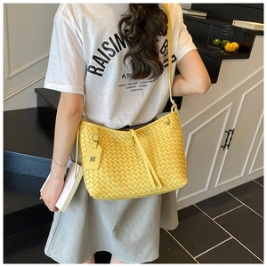 Detail of a bright yellow woven leather shoulder bag with metallic M charm and shoulder strap