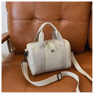 Détail d'un sac Boston beige avec ferrures en métal noir posé sur un canapé en cuir