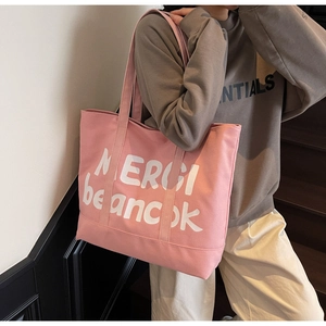 Detailed close-up of pink canvas tote bag with white MERCI letter printing and long strap