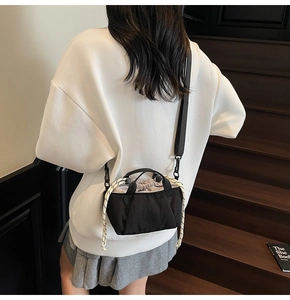 Detail shot of a black bucket bag with white rope accents worn by a model on stairs