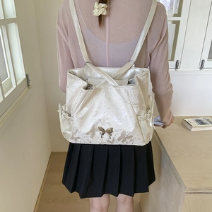 Detail of white backpack with silver butterfly buckles and drawstring side pockets
