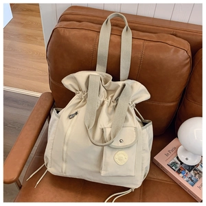 Close-up of beige drawstring tote bag with multi-pocket design on leather sofa
