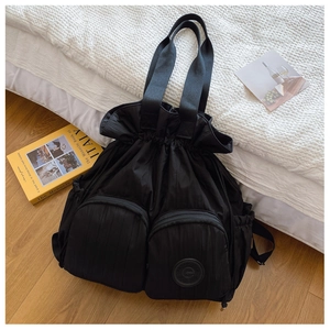 Detail of black pleated drawstring backpack with two front zipper pockets on white bedding