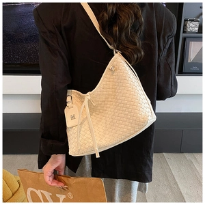 Detail of cream woven shoulder bag featuring leather M tag and drawstring closure on model