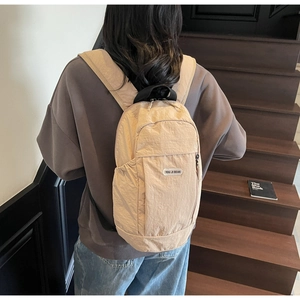 Detail of light khaki nylon backpack featuring durable zip pockets and brand rubber logo