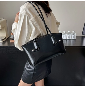 Sac sous le bras noir brillant avec détail argenté porté par un mannequin en studio