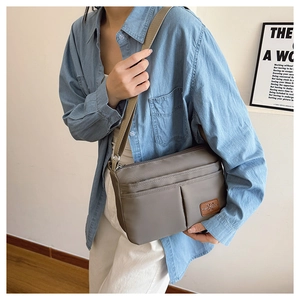 Detail of grey nylon crossbody bag with multi-zipper pockets on a denim shirt model