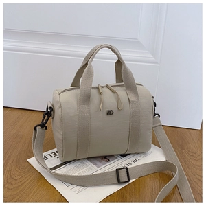 Détail d'un sac Boston en nylon beige avec logo métallique et bandoulière réglable