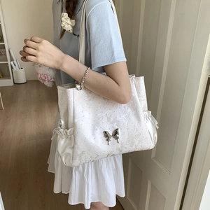 Detail of white jacquard tote bag with silver butterfly accent and side drawstring design