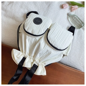 Detail of the pleated fabric texture and ruffled drawstring design on a white backpack