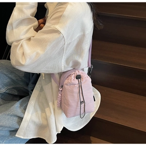 Sac bandoulière mauve en toile imperméable porté par un mannequin près d'un escalier