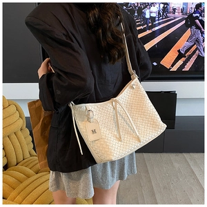 Close-up of white woven leather crossbody bag with letter M tag in an urban setting