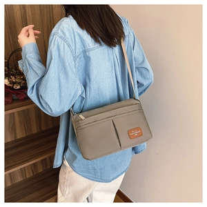 Detail of khaki nylon crossbody bag showing the front zipper pocket and leather logo tag