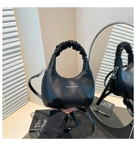 Gros plan du sac en croissant noir avec cuir grainé et détail de poignée plissée