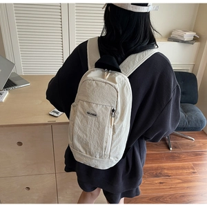 Close-up of lightweight cream nylon backpack featuring brand tag and zip front pocket
