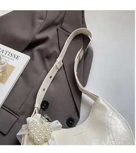 Detail of cream pleated leather hobo bag with pearl heart charm on a brown blazer