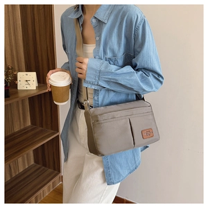 Detail of grey canvas crossbody bag with brown leather label and wide shoulder strap