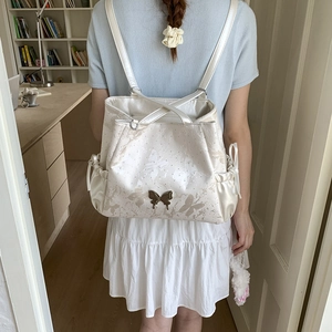 Detail of white backpack featuring delicate butterfly prints and metal butterfly charm