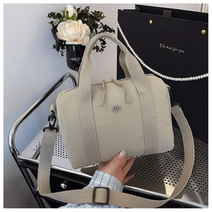 Détail du sac boston en nylon beige avec poignées tissées et emblème logo argenté
