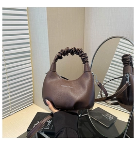 Détail du sac à main marron en cuir avec poignée plissée et texture grainée litchi