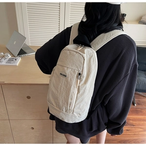 Detail of a beige nylon backpack with a zipper pocket and metal brand logo plate