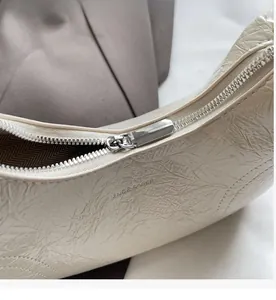 Detail of silver zipper and crinkled leather texture on cream underarm bag