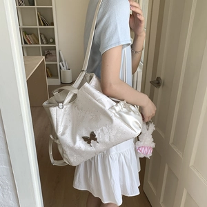 Detail of white satin tote bag featuring a metal butterfly logo and soft ribbon bow