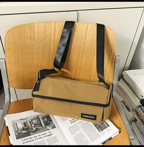 Détail d'un sac cylindrique en toile kaki avec fermeture éclair noire et bandoulière large