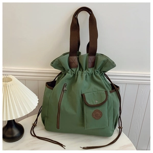 Detail view of a green canvas drawstring bucket bag with brown handles on a marble surface