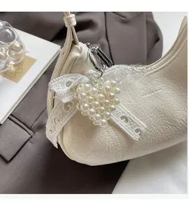 Detail view of cream shoulder bag with lace bow and pearl heart charm on a textured surface