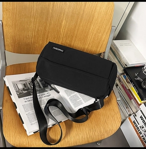 Gros plan détaillé d'un sac bandoulière cylindrique noir posé sur une chaise en bois