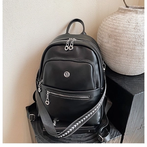 Detail of black faux leather backpack featuring textured wide strap and silver metal logo