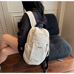 Minimalist beige backpack shown from side view on a model in a cozy indoor setting
