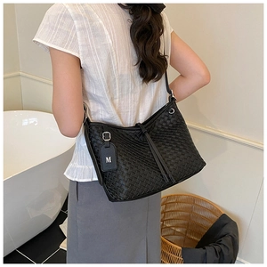 Detail of black woven tote bag featuring a leather tag with a silver M logo on a model