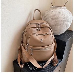 Close-up of light brown faux leather backpack with textured straps and multi-pocket detail