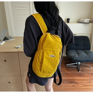 Detail of yellow nylon backpack featuring a white brand label and black zipper closure