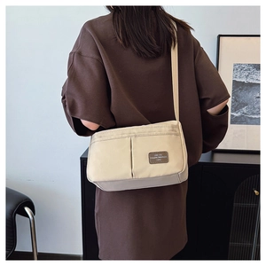 Close-up of beige nylon crossbody bag with adjustable wide strap and front logo patch