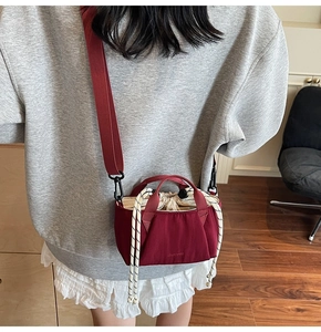Detail view of burgundy nylon bucket bag with drawstring and woven strap on model