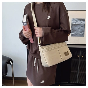 Detail of cream canvas crossbody bag with adjustable strap worn with casual brown outfit