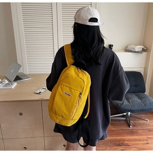 Detail view of the yellow nylon mini backpack featuring a silicone brand patch and zippers