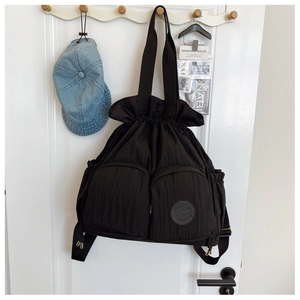 Detail of black drawstring tote bag with crinkled nylon fabric and front zipper pockets