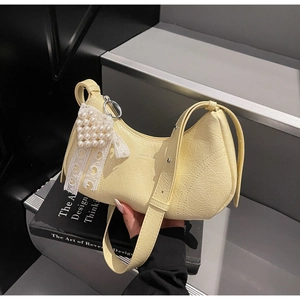 Detail of a light yellow crescent bag with pearl heart charm and lace bow details