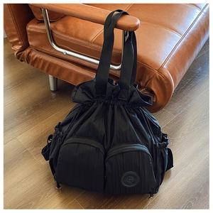 Detail of black nylon drawstring backpack with front zip pockets on leather sofa
